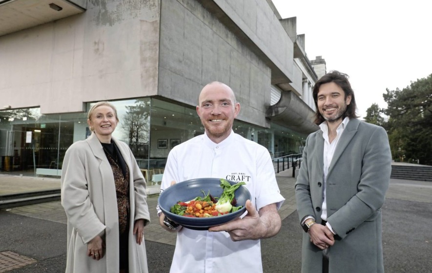 Three individuals pictured outside Ulster Museum, one is a chef holding a dish of food
