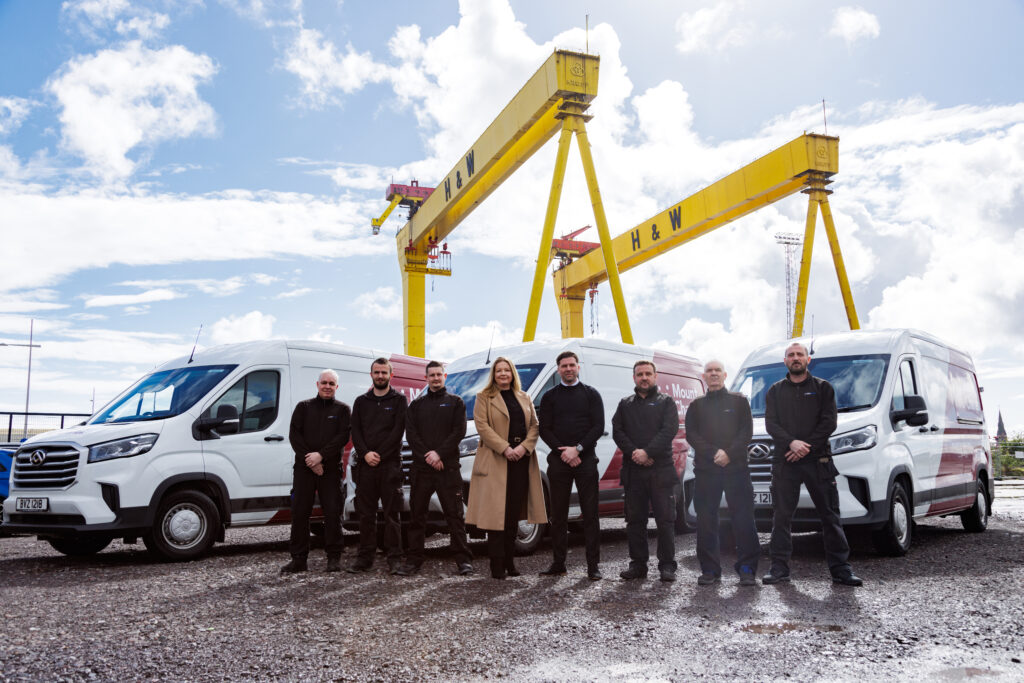 The MC vending and distribution team standing at Harland and Wolff with MC branded vans and H&W cranes in the background