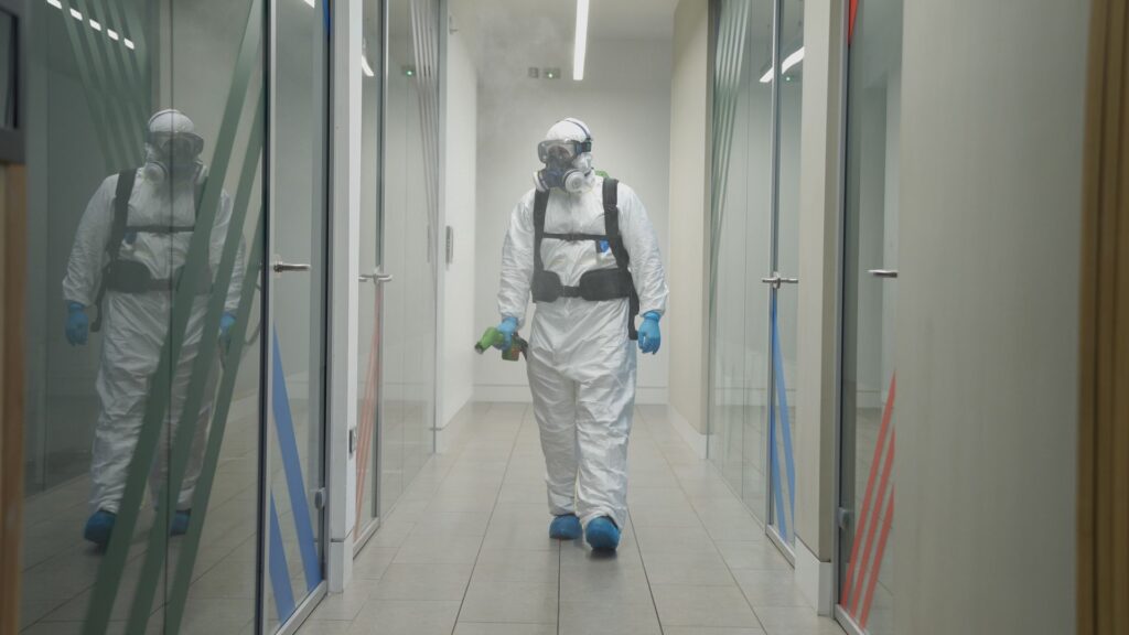 A cleaning operative walks through office space in full PPE