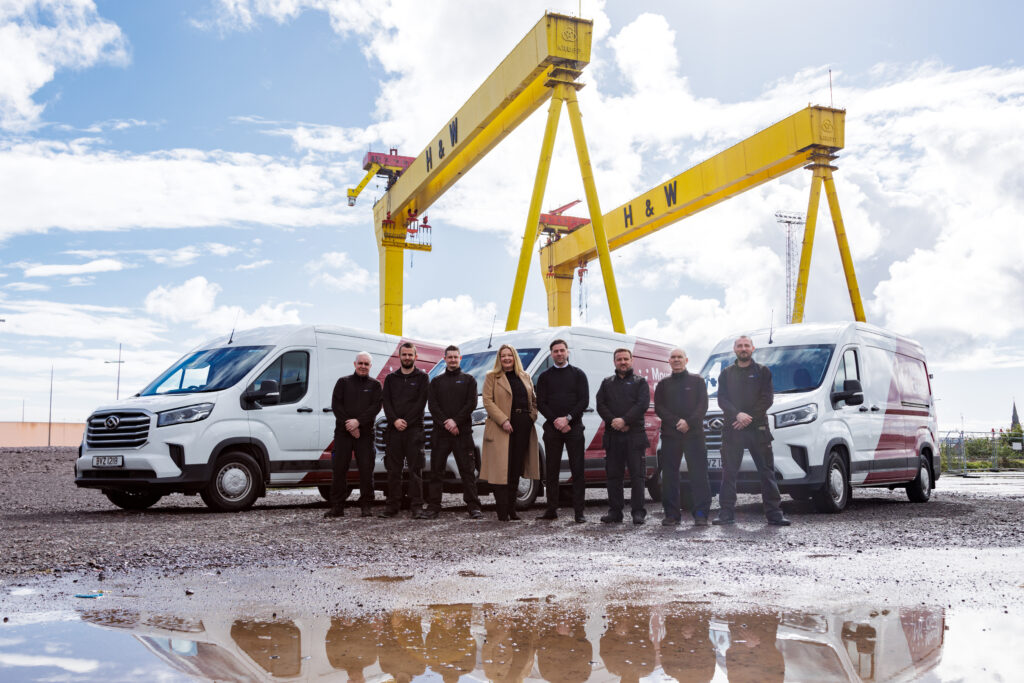 Vending and distribution team stand in front of MC branded vans and H&W cranes